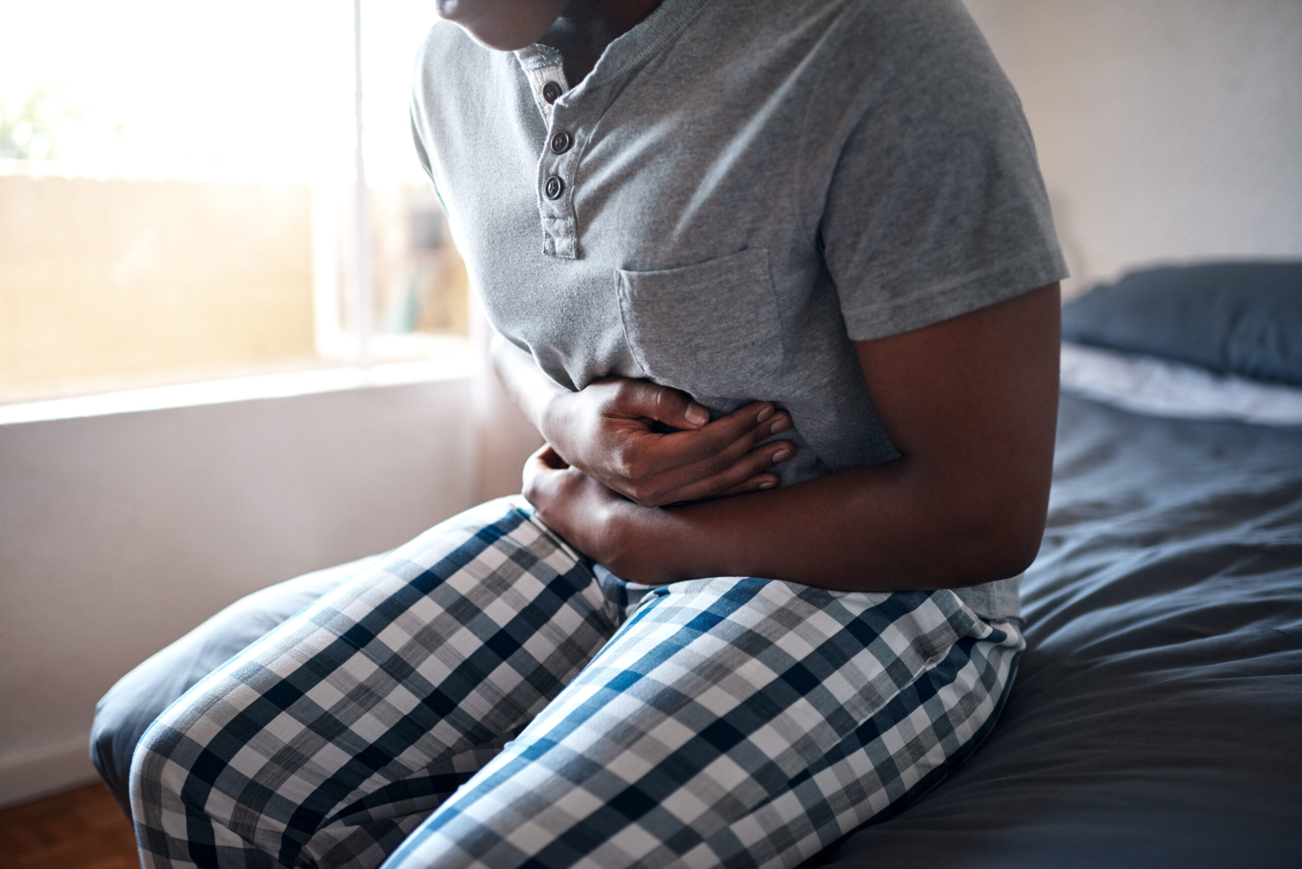 Person sitting on bed, holding stomach, experiencing abdominal pain. Possible allergy symptom.