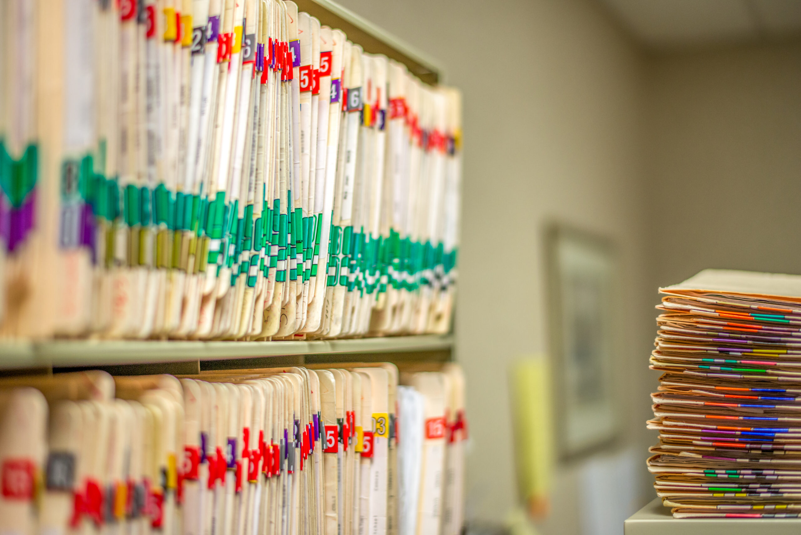 Rows of medical files organized on shelves, with a stack of files in the foreground.