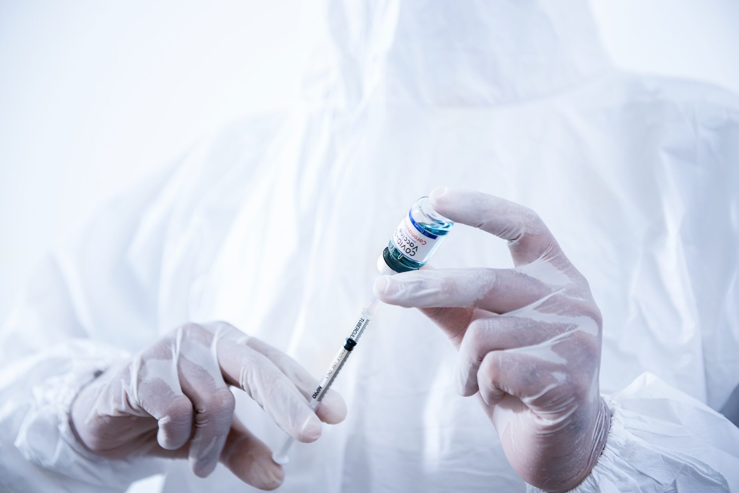 Close-up of gloved hands preparing a COVID-19 vaccine injection.