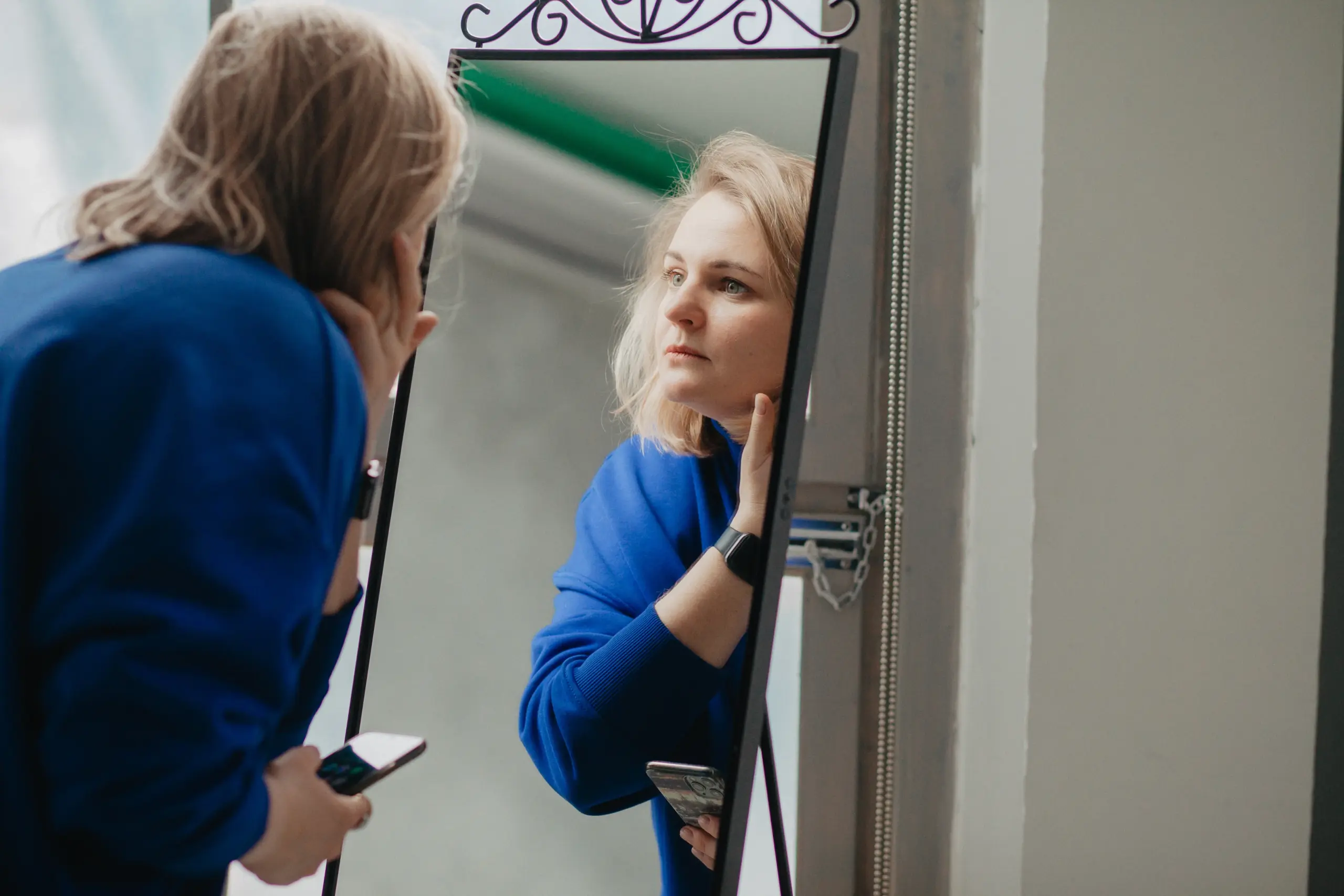 Woman looking in mirror, considering anti-aging hormone treatment.