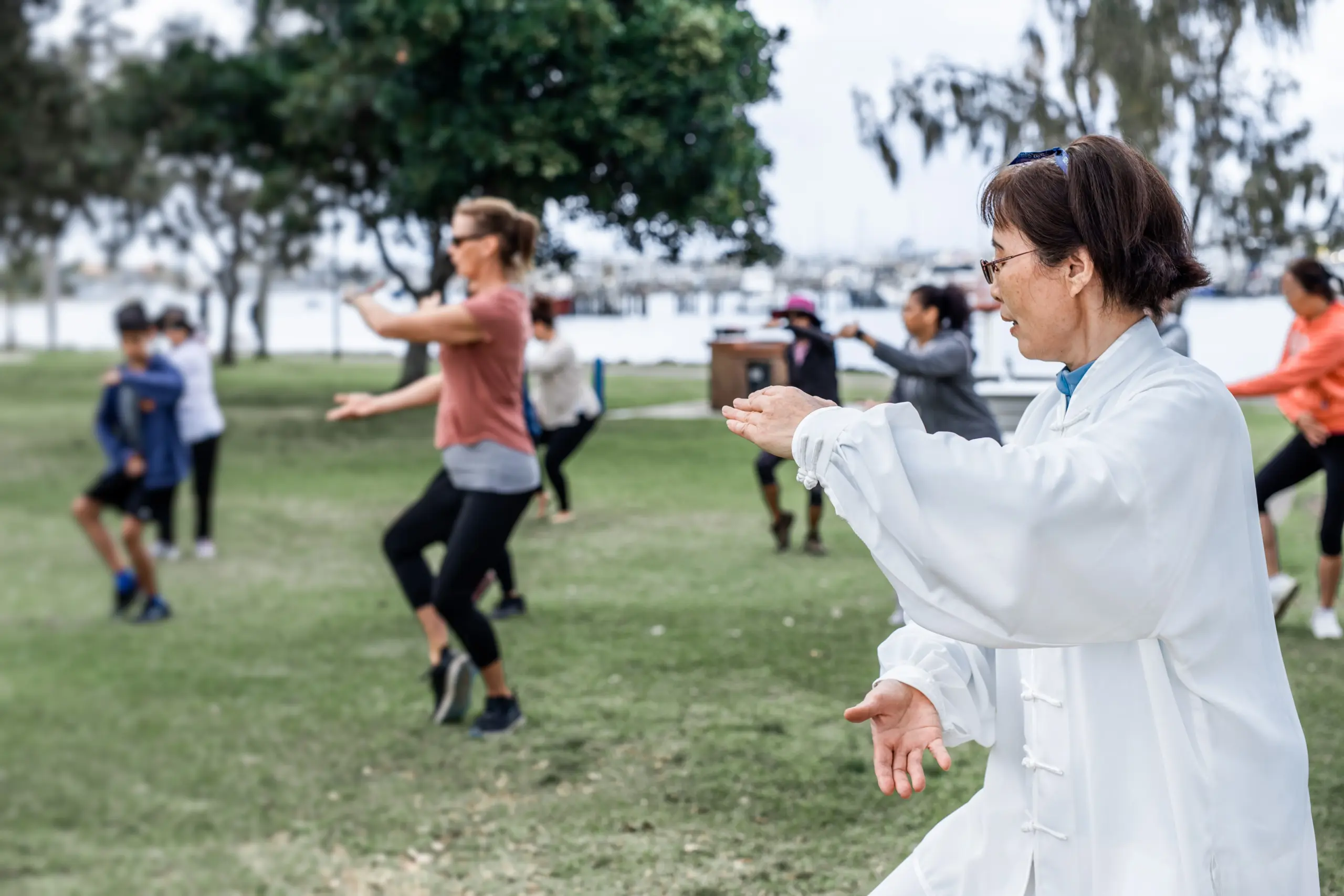 Tai Chi class in a park. People of all ages practice gentle movements.