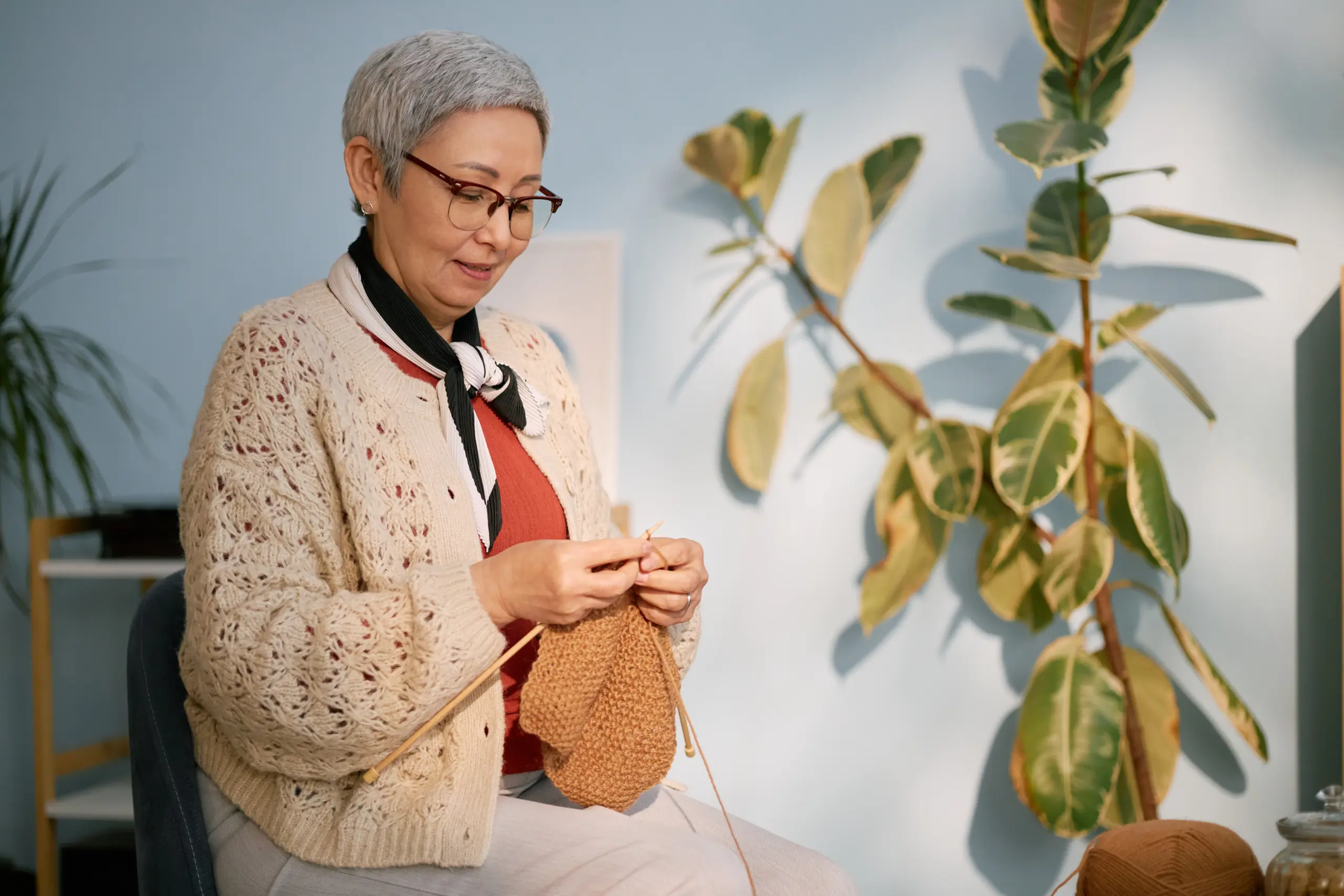 Senior woman knitting a brown sweater. Relaxing hobby.