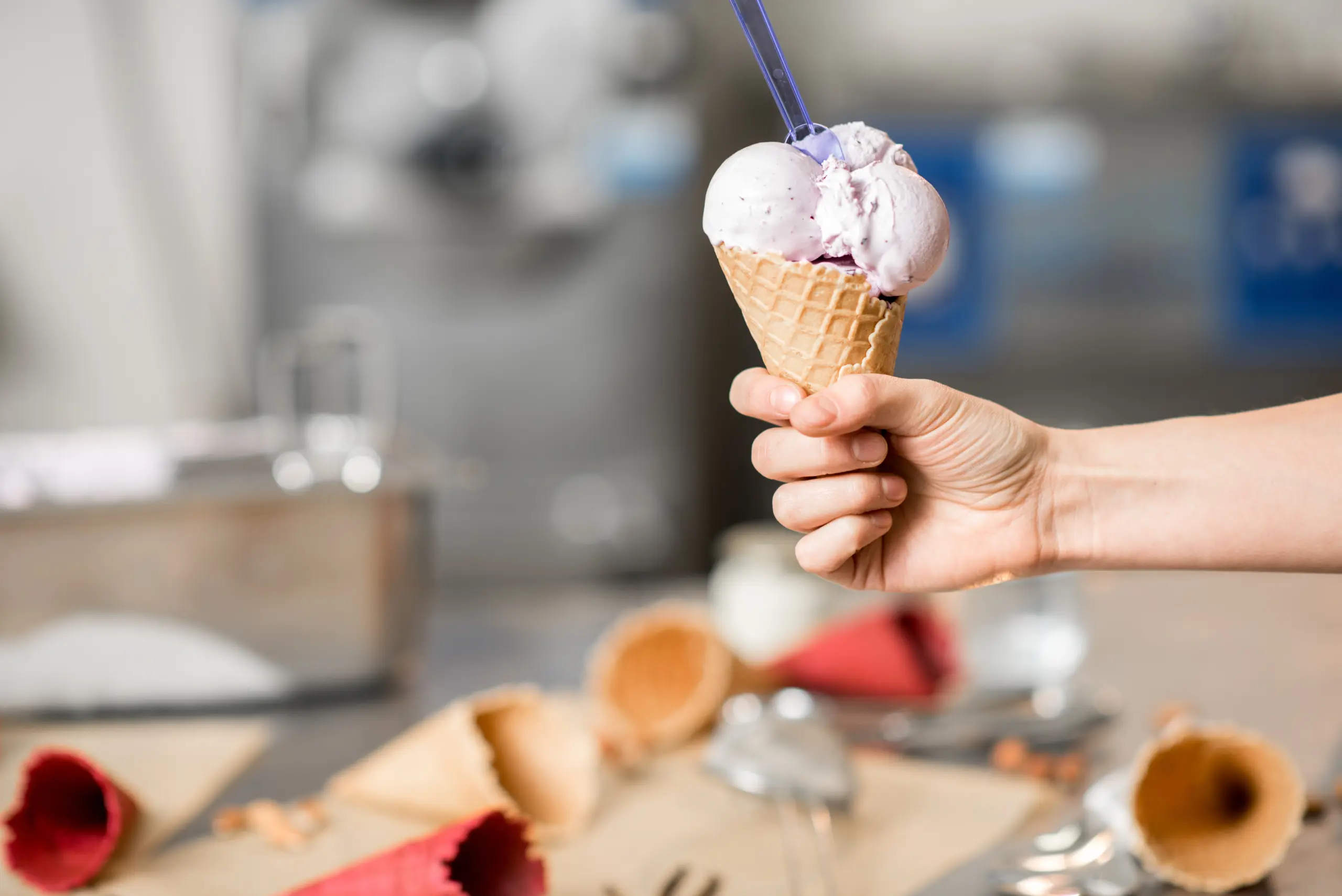 Close-up of a hand holding a waffle cone filled with scoops of purple ice cream.