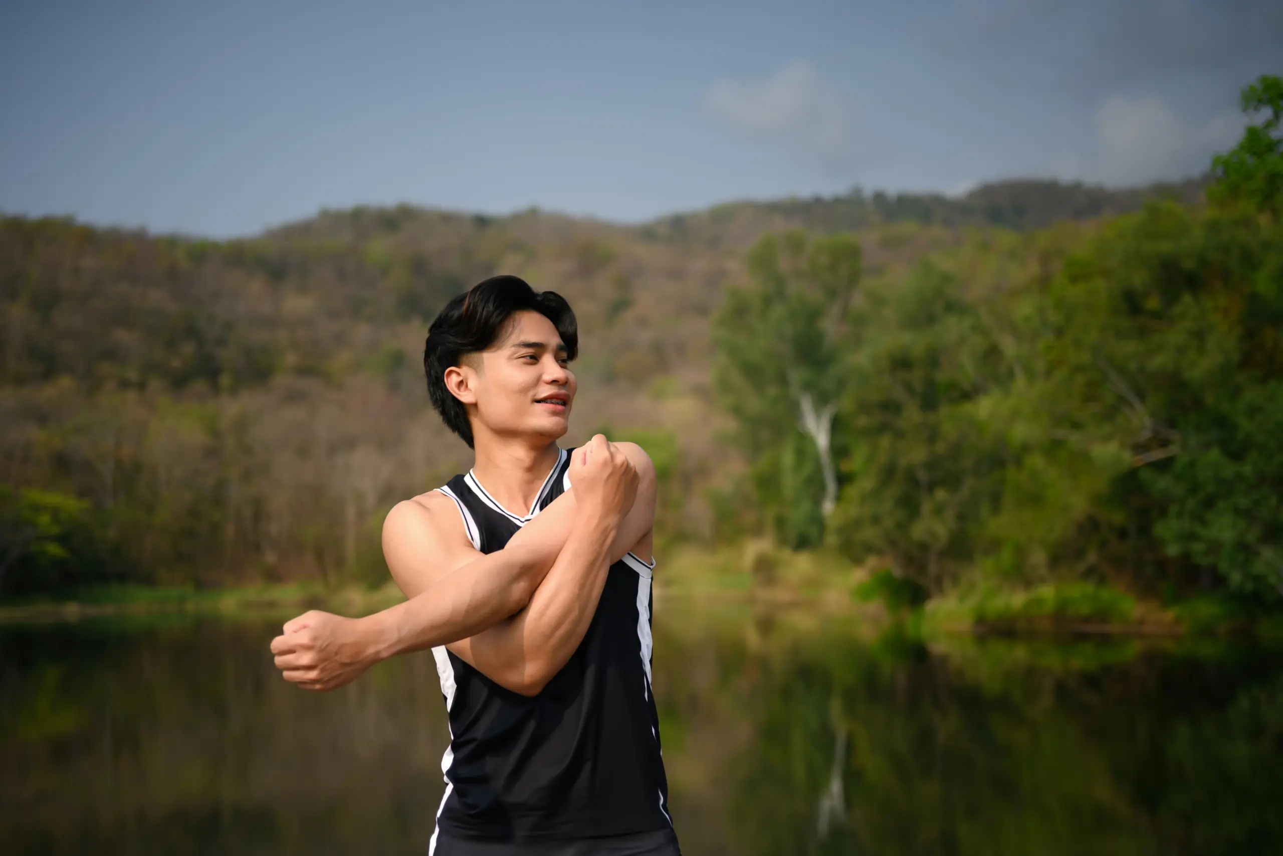 Man stretching his arms outdoors near a lake.