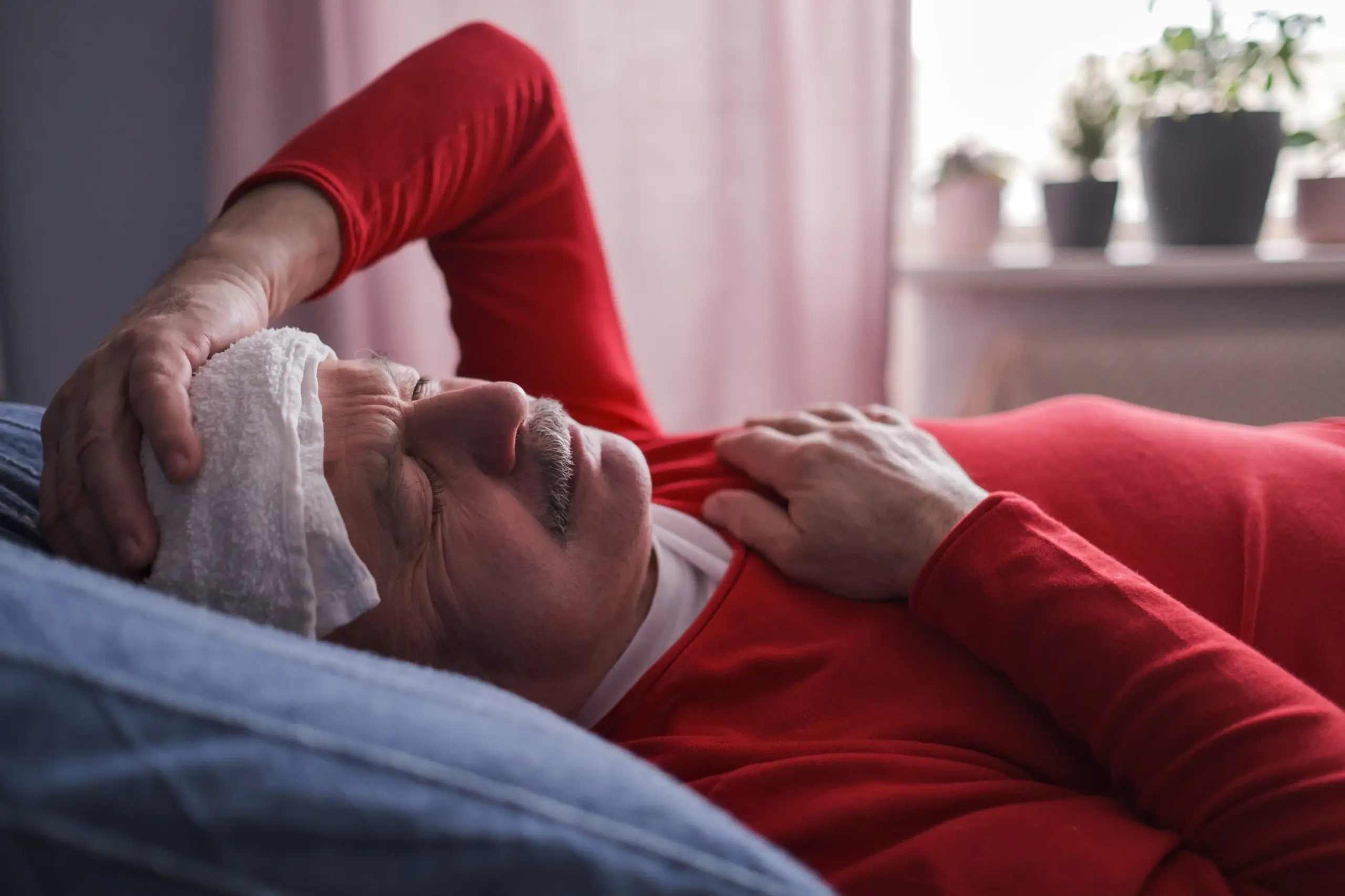 Elderly man resting in bed with a cool compress on his forehead.