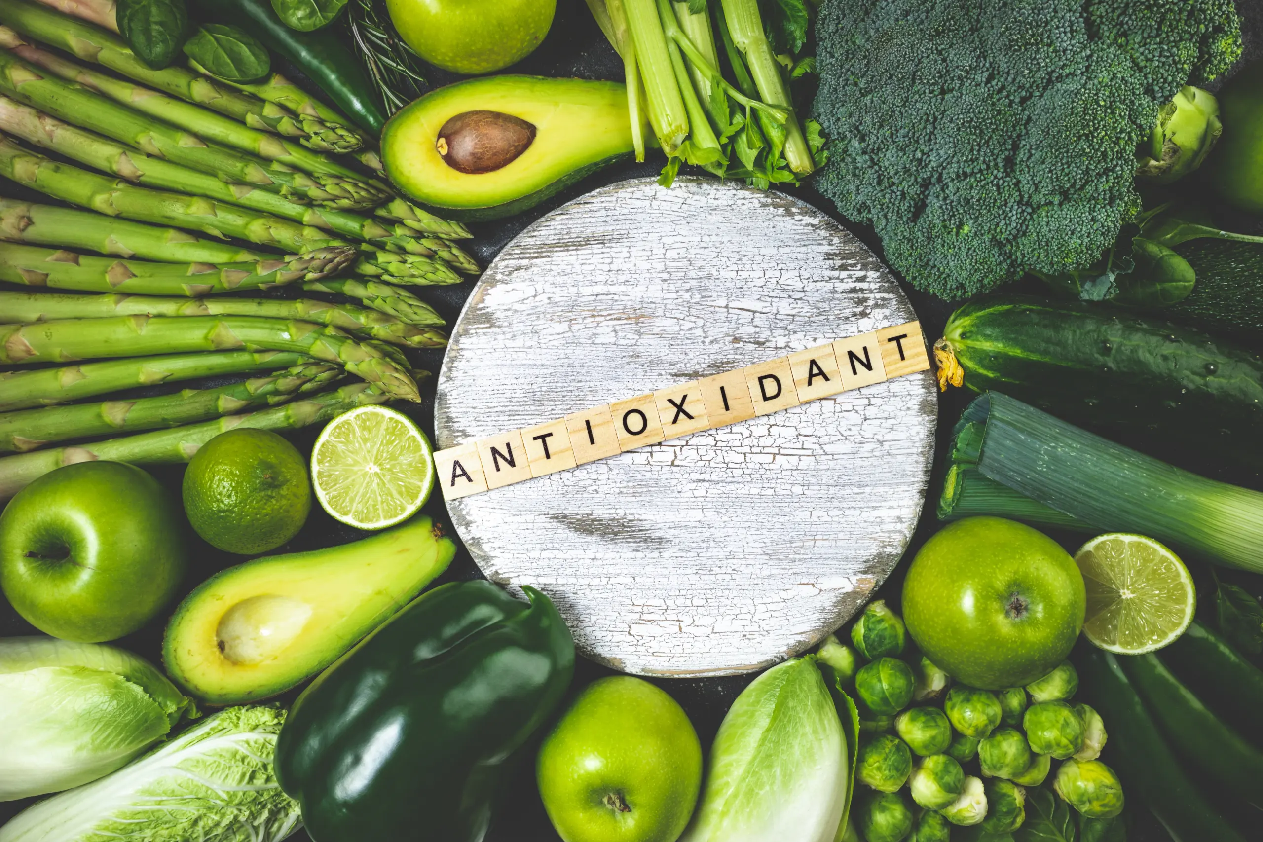 Assortment of green fruits and vegetables arranged around a board with the word ANTIOXIDANT spelled out.