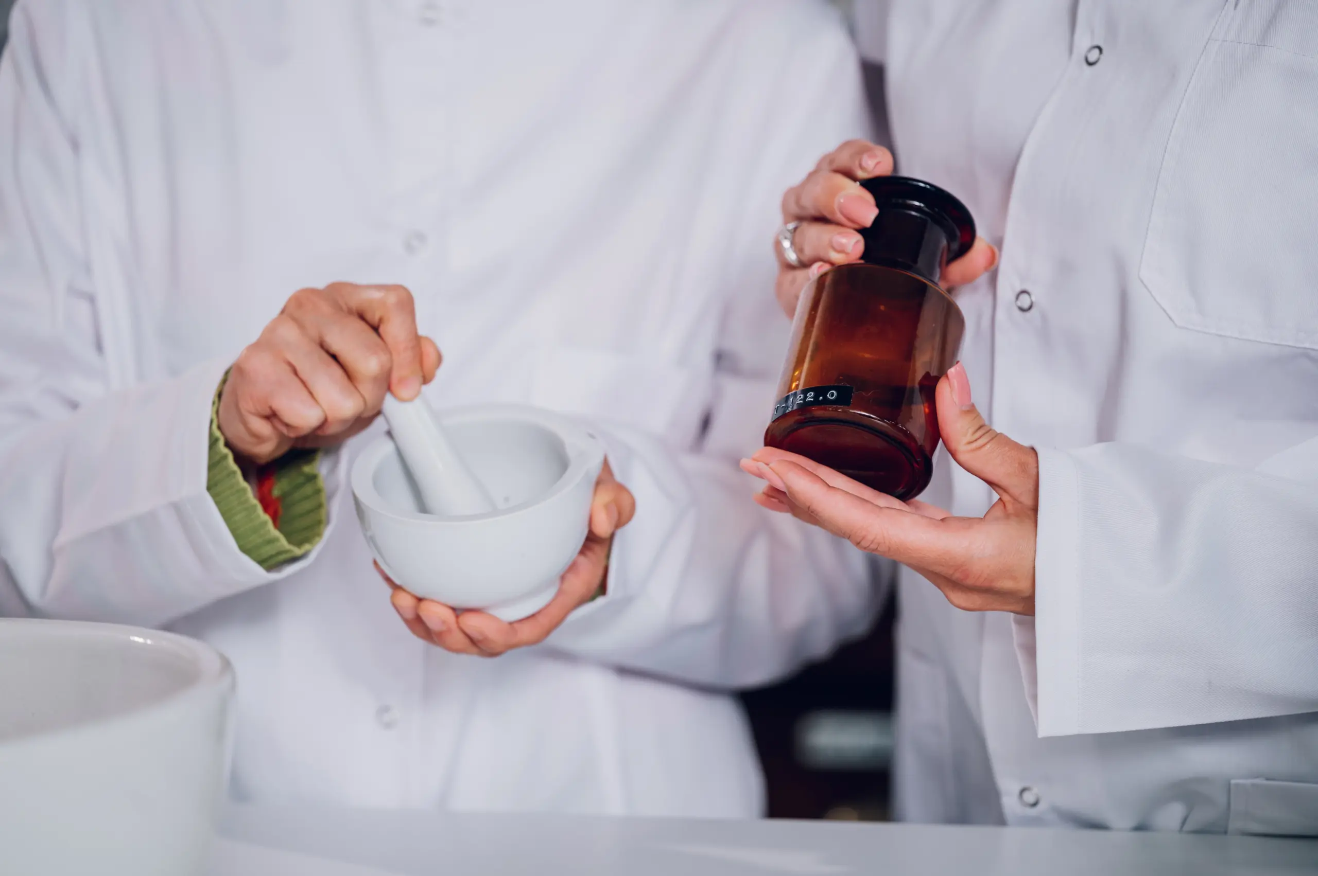 Pharmacists preparing medication using mortar and pestle and amber bottle.